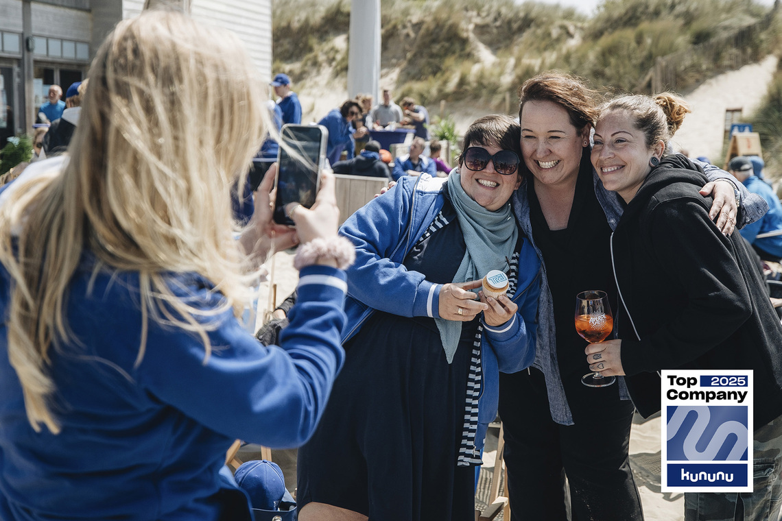 Drei lachende Frauen auf Trei Team Event werden von einer weiteren fotografiert. Rechts unten: Kununu Top Company 2025 Siegel 